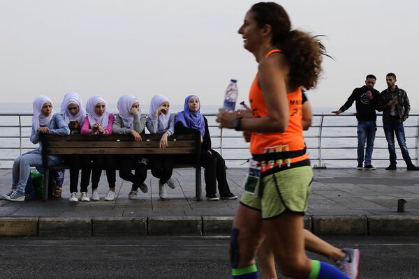 Девушки в хиджабах наблюдают за участницей городского марафона на набережной в Бейруте, Ливан - Sputnik Молдова